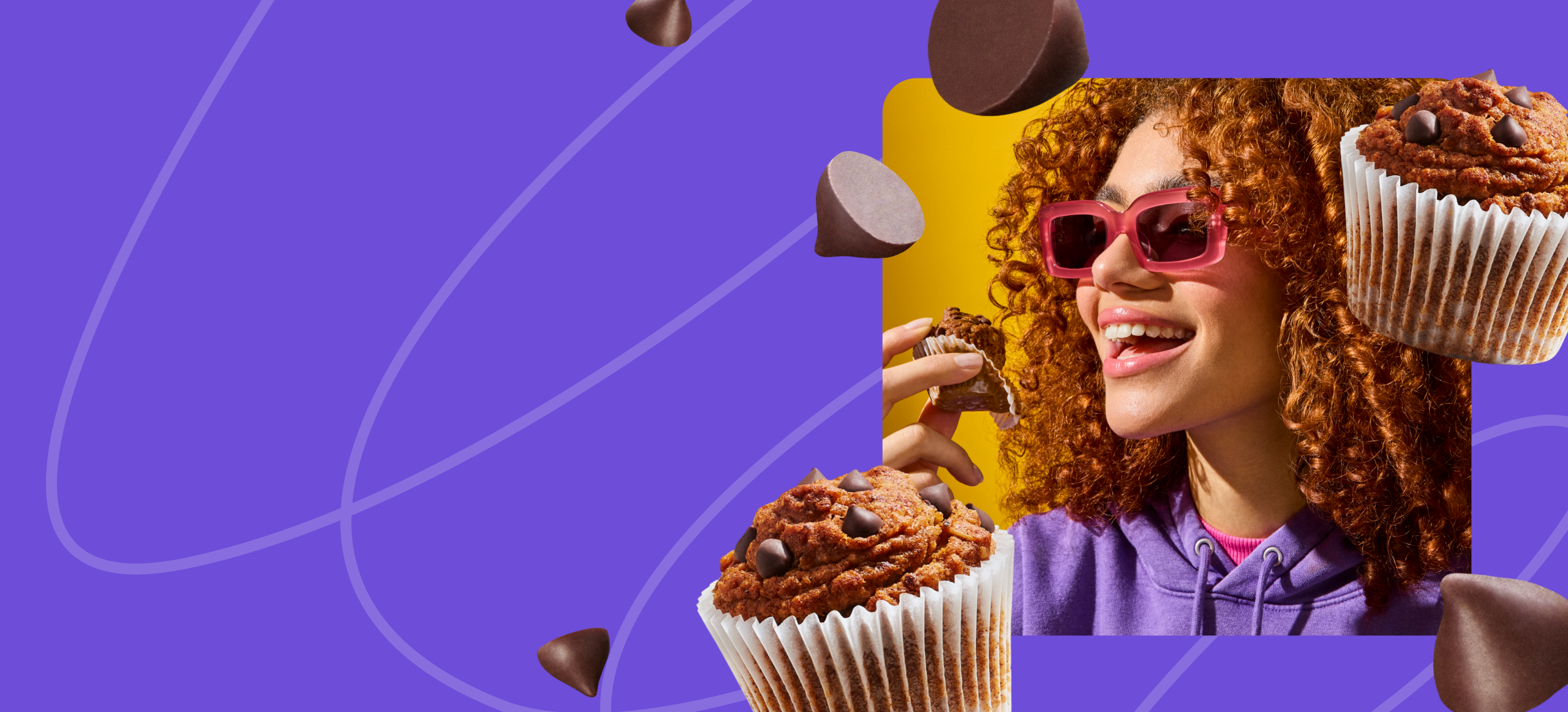 A young woman with voluminous curly red hair and pink sunglasses smiles as she holds a Mornings Oat Cup in a paper wrapper. She is wearing a purple hoodie and a pink turtleneck, with a bright yellow background adding vibrancy to the image. The scene exudes joy and indulgence.