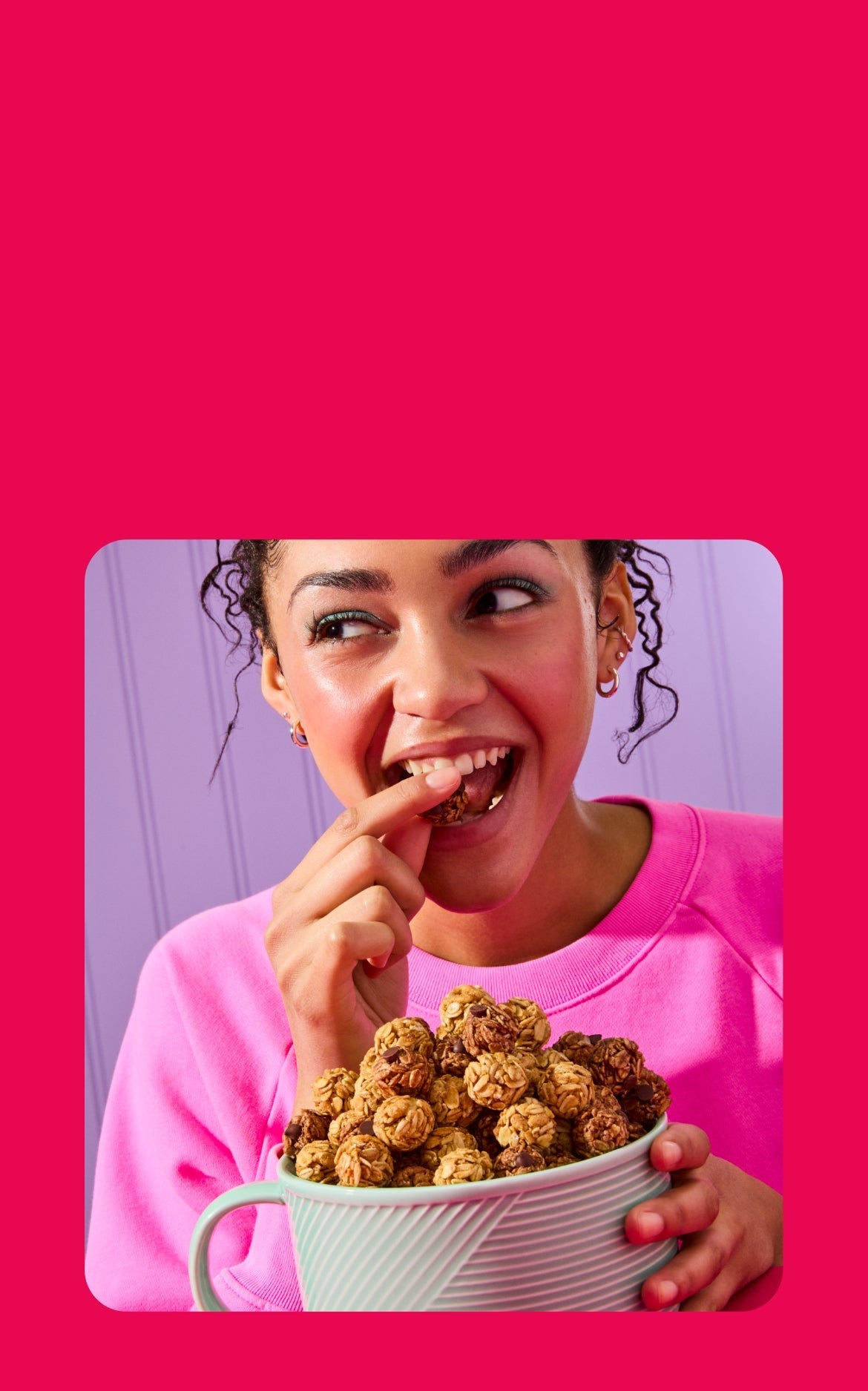 A bold and colorful promotional image featuring a smiling woman in a pink sweatshirt enjoying a bite-sized oat and chocolate snack. Surrounding her are floating snack bites, highlighting their texture and ingredients. A purple speech bubble with large, playful text reads, "Pop it. Share it." Below, white text on a red background emphasizes, "Organic snacks you’ll wanna share." The composition is fun and energetic, reinforcing the snack’s appeal.