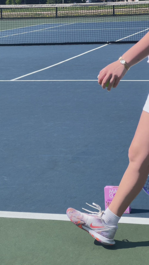 A woman walks across a tennis court with a box of MadeGood Birthday Cake Drizzled Granola bars on court. Transitions to her seated on a park bench eating the mornings bar.